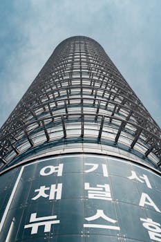 Tall glass skyscraper in Seoul with Korean script, showcasing modern architecture.