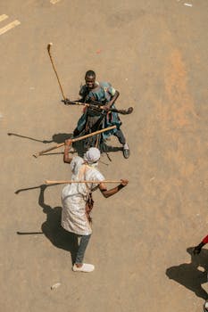 Two individuals engage in traditional stick fighting outdoors, showcasing cultural heritage.